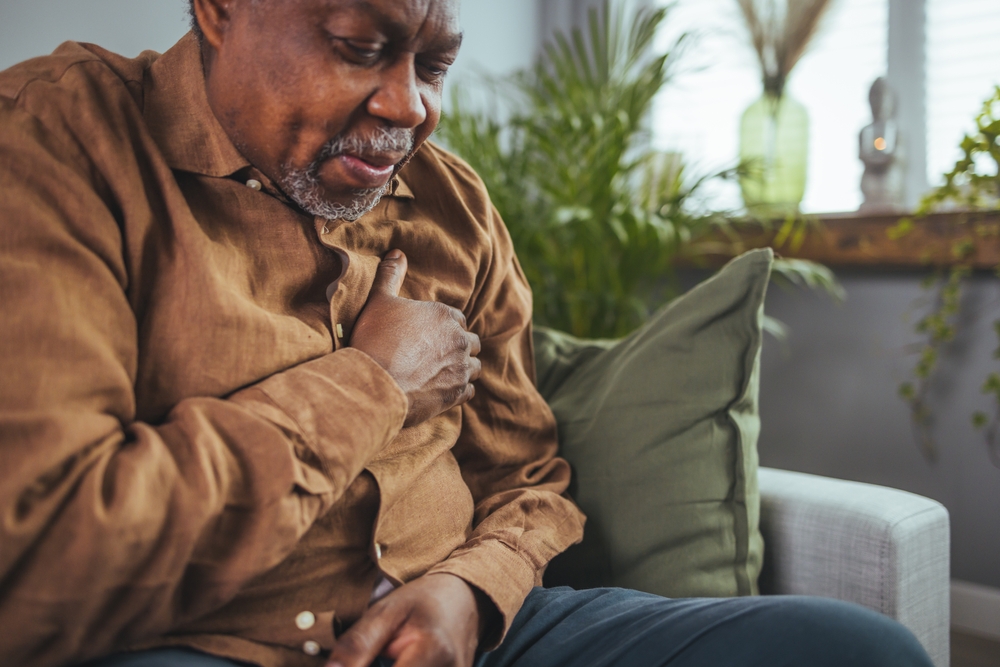 A man sits on a couch clutching his chest