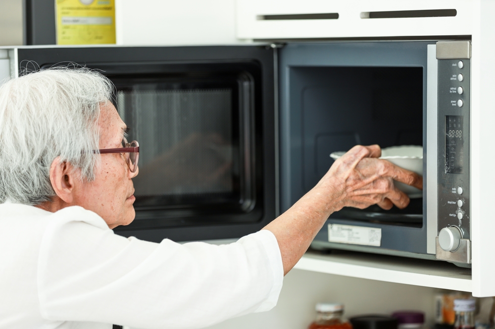 An elderly person places a plate into a microwave oven.