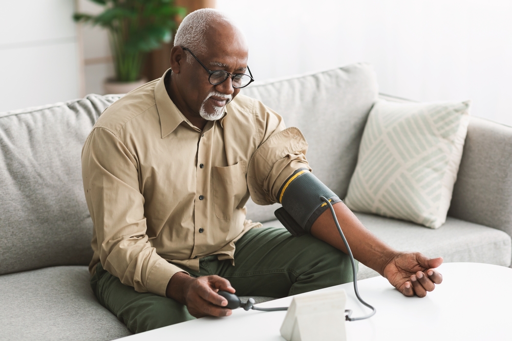 An elderly man with glasses checks his blood pressure using a monitor