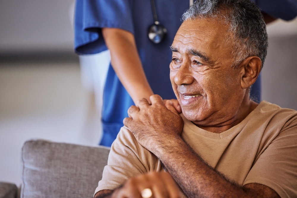 An elderly man smiles while receiving comforting support from a professional care giver