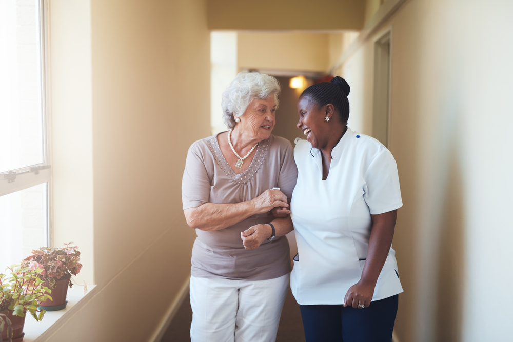 An elderly woman and a nurse walk down a hallway