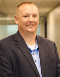 A man wearing a dark blazer over a light blue polo shirt stands in an indoor setting, smiling at the camera, representing personal care services.