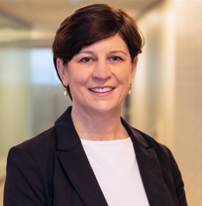 A woman with short brown hair is smiling while wearing a black blazer and white shirt in an indoor, well-lit setting, reflecting her dedicated role in home health care service.