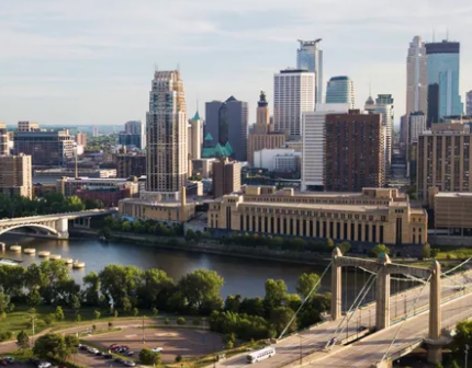 Aerial view of a cityscape with tall buildings, a river, bridges, and several green areas on a sunny day, showcasing the harmony between urban life and nature, reminiscent of how elder home care services bring balance to busy lives.