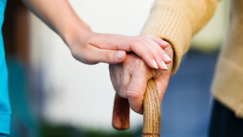 A younger hand rests gently on the hand of an older person who is holding a walking cane, embodying the essence of elder home care services.