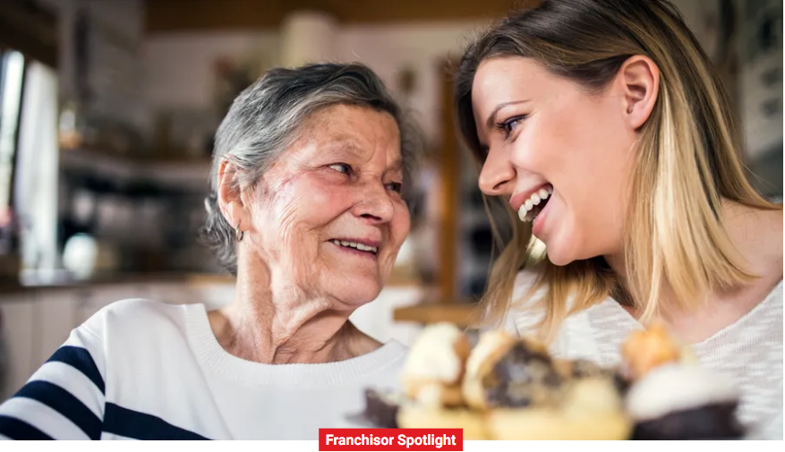 A smiling elderly woman and a younger woman, exemplifying the essence of home care, share a moment at a table with dessert in the foreground.