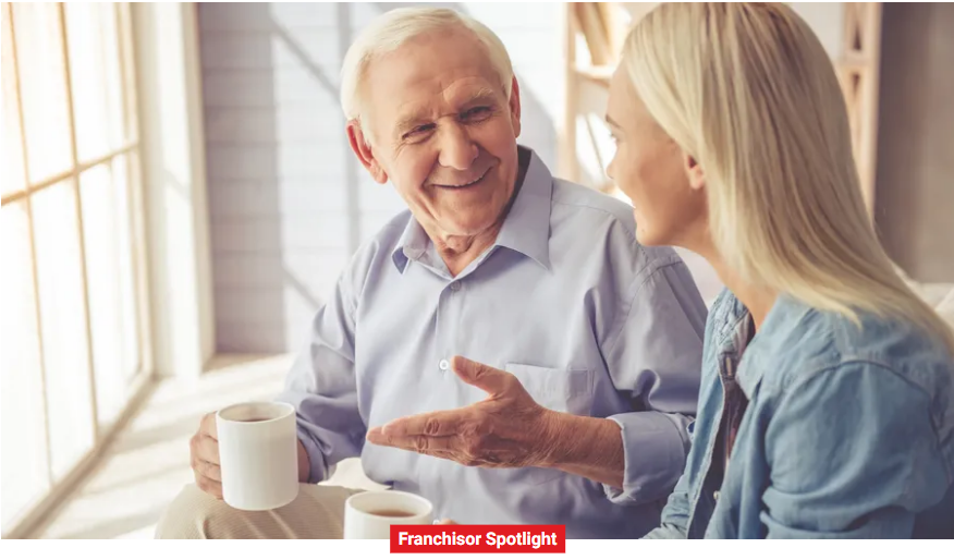 An elderly man and a younger woman sit by a window, smiling and drinking coffee. "Franchisor Spotlight" text is displayed at the bottom, highlighting excellence in home health care service.