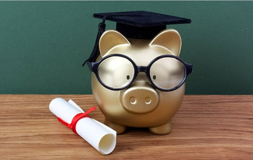 A piggy bank wearing a graduation cap and glasses sits on a wooden surface next to a rolled diploma tied with a red ribbon, symbolizing the importance of education and preparation—much like how care pairing ensures the right caregiver services for those in need.