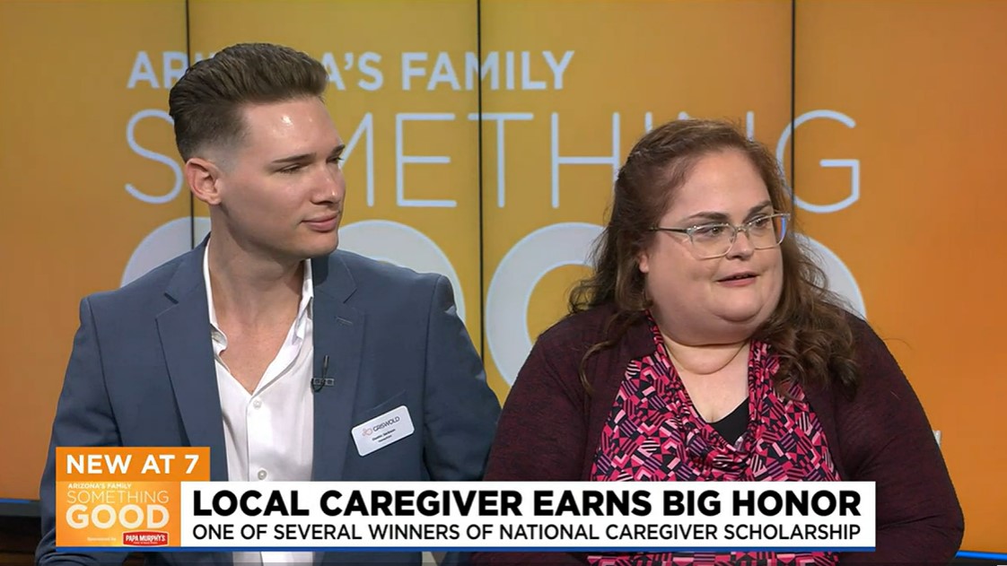 Two people sit side by side on a television set. The text states, "Local caregiver earns big honor," referring to a national caregiver scholarship award for excellence in elder home care services.