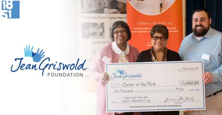 Three individuals are holding a large check for $1,000 from the Jean Griswold Foundation, which supports elder home care services. The foundation's logo is visible on the left side of the image.