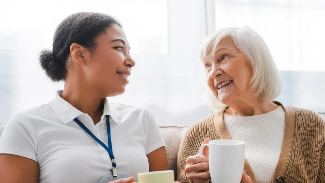 A young care giver shares a conversation and smiles with an elderly woman