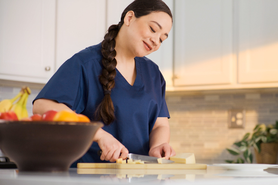 Person in a blue shirt slicing cheese on a cutting board in a kitchen.