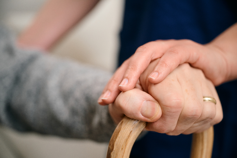 A person with a ring gently holds another person's hand resting on a wooden cane.